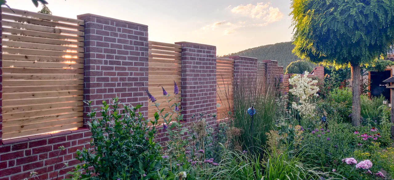 Sichtschutzzaun im Garten aus Kombination mit Holz-Sichtschutz und Klinkermauer im klaren rotton. Mit der grünen Bepflanzung eine schöne klassische dennoch modern wirkende mauer