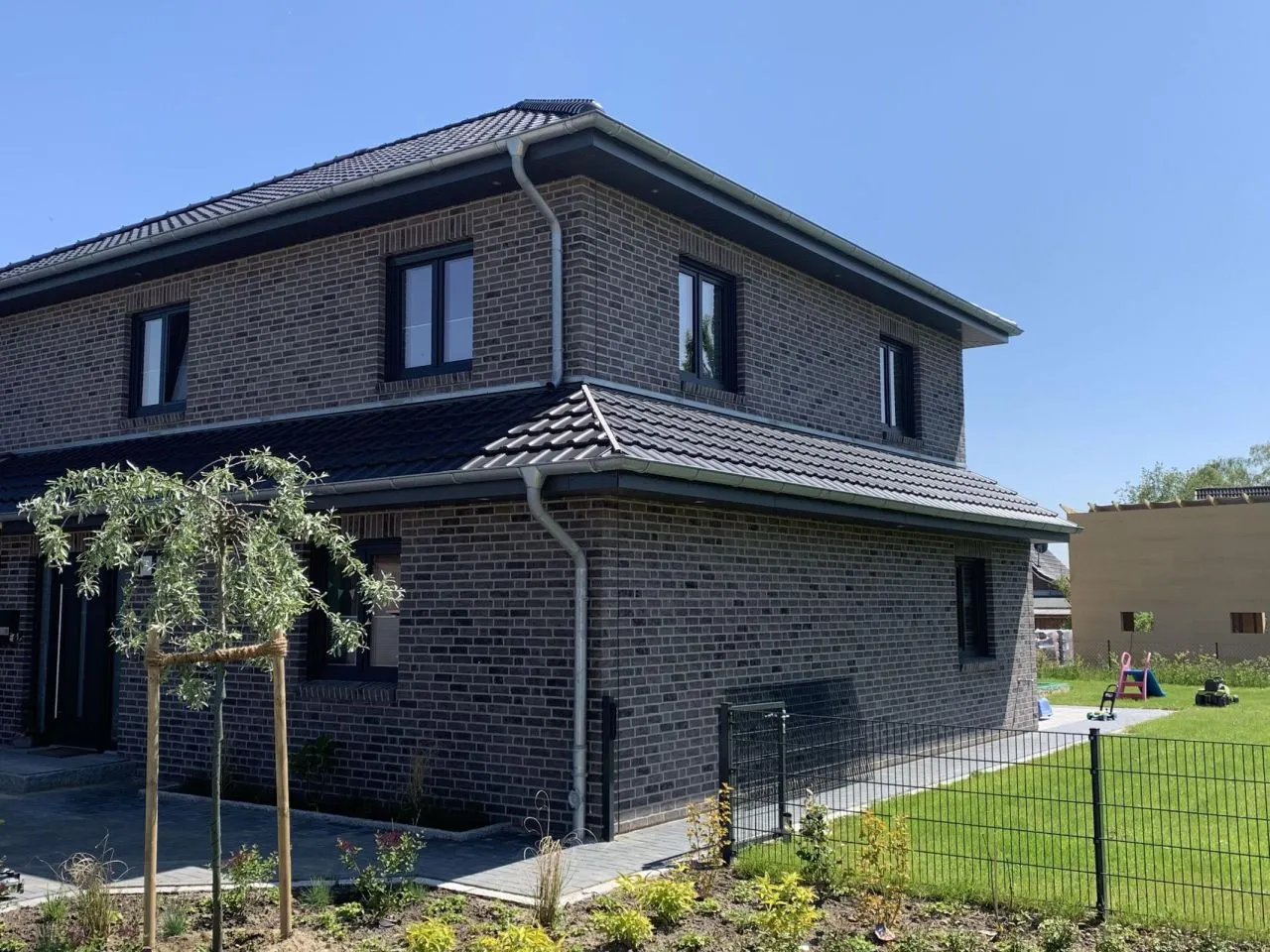 Hausfassade eines modernen Hauses mit dunkel grauaen Fenstern und Dach. Die Riemchen der Sorte Wolf grey in grau, braun wirken dunkel modern und dennoch zeitlos. es kommen die grauen als auch die braunen steine gut zur Geltung