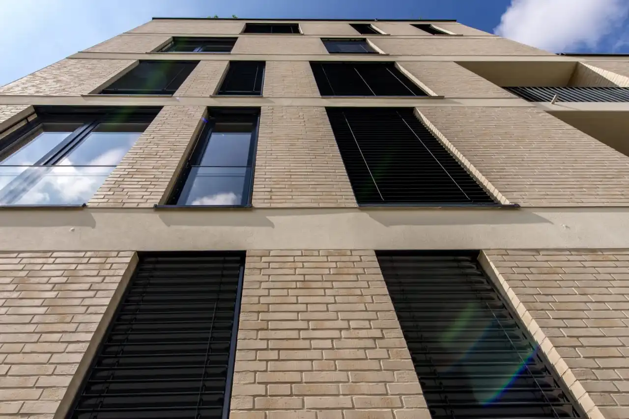 Ansicht eines Wohngebäiudes mit mehreren Etagen und dunklen Fenstern mit gelber Fassade