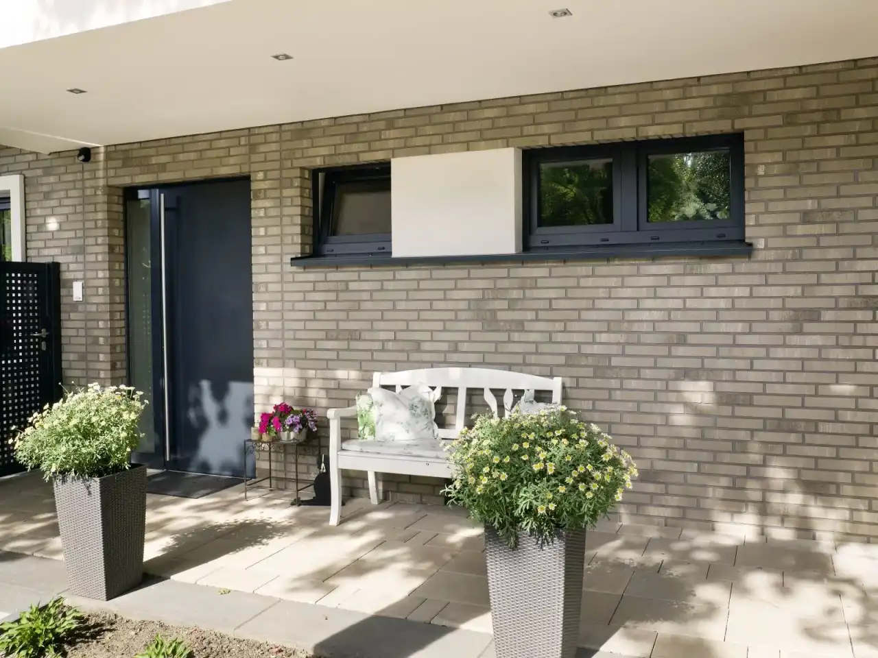 Eingangsbereich mit dunklen Fenstern und grau beigen Riemchen als Hauswand