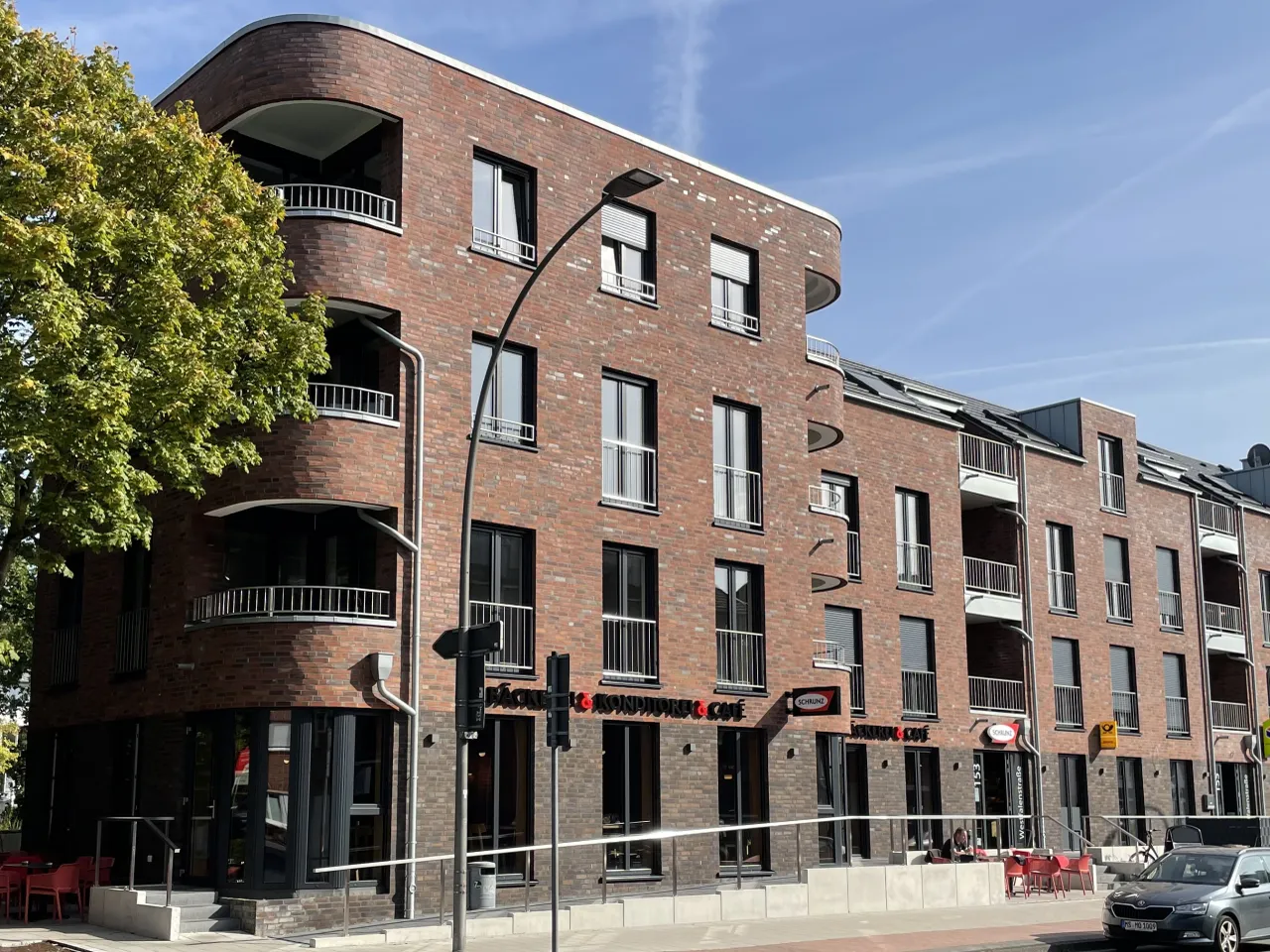 Viergeschossiger Flachdachbau mit roten glatten Klinkerriemchen ab dem ersten Geschoss. Das Untergeschoss ist mit einem braunen Klinker verkleidet. Viele Fenster.