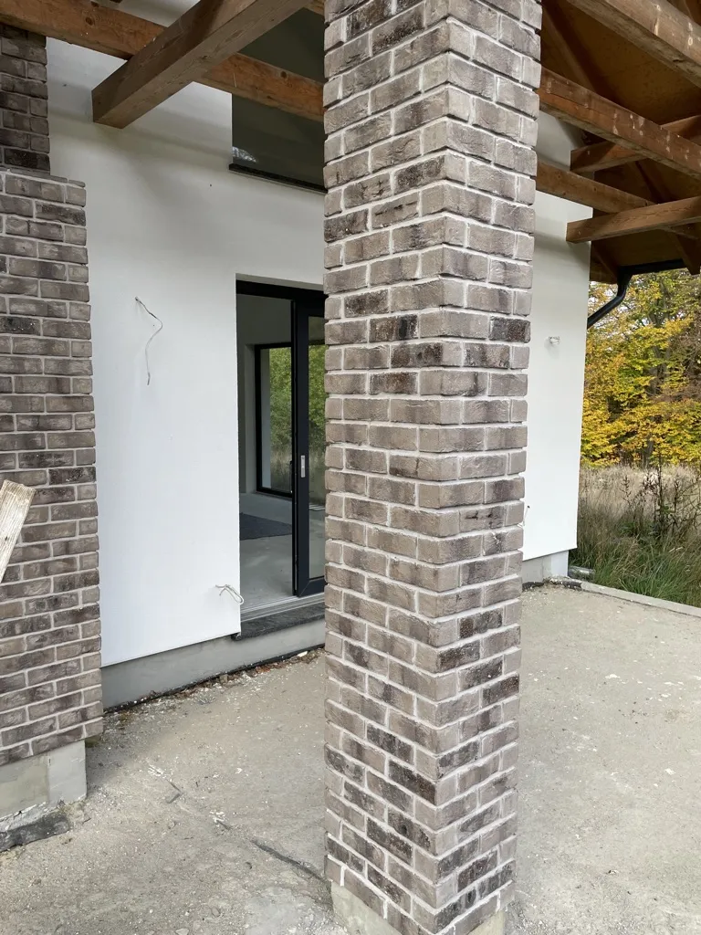 Eckige Säule mit der Sorte Lava in grautönen im Außenbereich. Modern und besonders durch den Schmolz auf den Riemchen