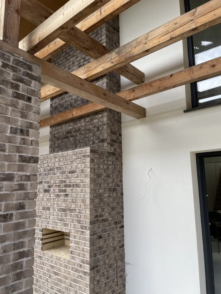 Outdoor-Pizzaofen der zum Kamin übergeht. Die in grau gehaltenen Riemchen passen toll zu der weißen Hauswand und den Holzbalken. Eine graue, moderne Wand mit der Sorte Lava