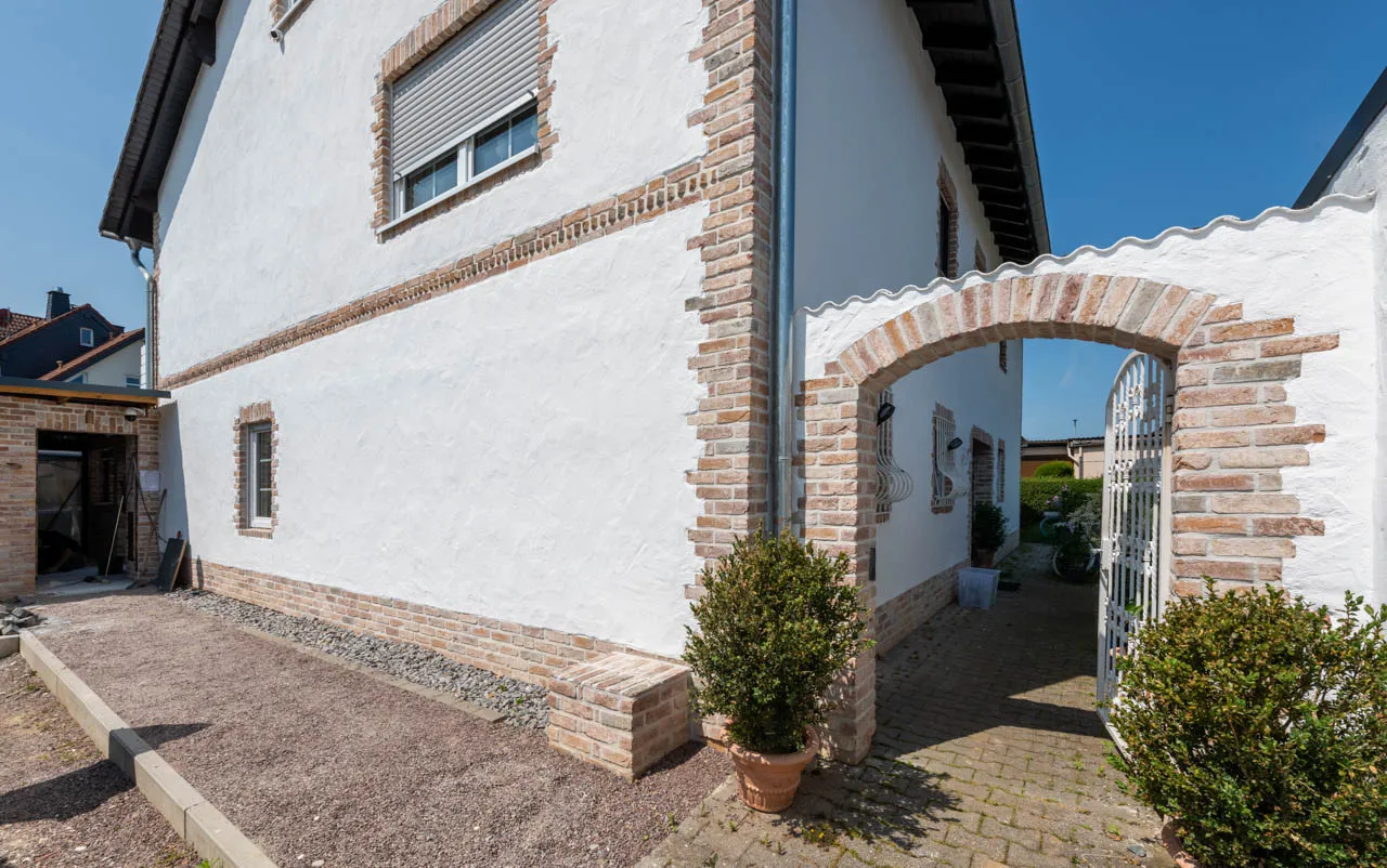 Haus weiß verputzt mit Kombination Backsteinriemchen Mediterran Finca und umrahmter Eingangsbogen