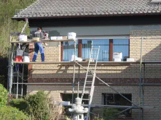 Baustellt mit verklinkerten Haus und Gerüst vor dem Haus. Ein Mann verarbeitet gerade Riemchen an dem Haus