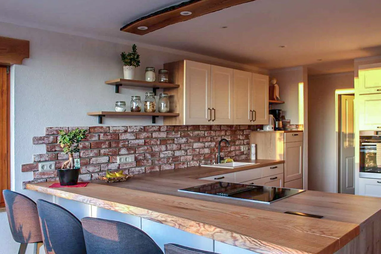 Klinker-Küchenrückwand mit rot-bunten Backsteinriemchen mit weißem Kalk geschlämmt. Die Wand passt durch die schlämme gut zur weißen küchenfront. zudem hebt sich das rot gut von der holzarbeitsfläche ab. ein tolles harmonisches gesamtbild