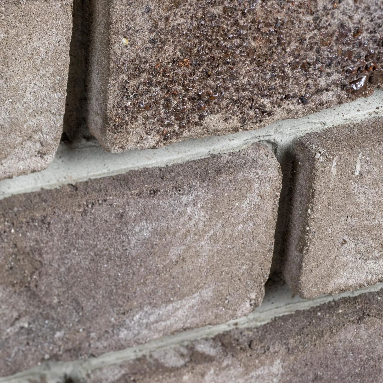 Produktbild schräg im Detail Klinkerriemchen Lava. Ein graues Riemchen mit Schmolz. Quasi Geschmolzener Stein zum ANfassen. Die Oberfläche ist genarbt und fein hell besandet
