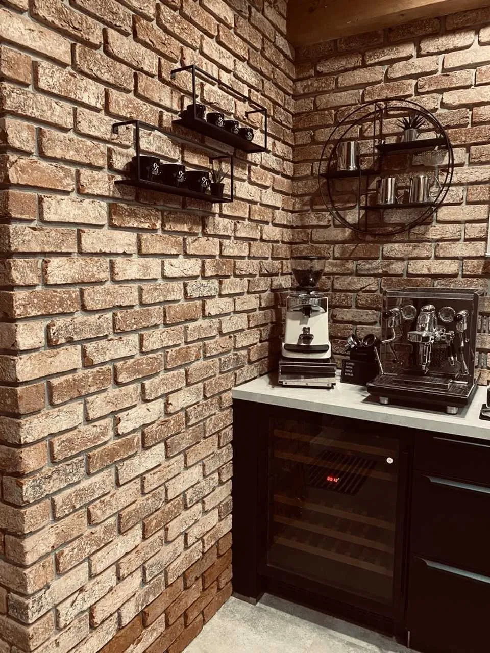 Backsteinwand in der Küche. Die mit roten Klinkerriemchen wirkt hier durch die geblich und schwarze Besandung etwas dunkler. Die Küche und Deko ist in schwarz gehalten. EIn schöner Kontrast zu dem edlen Rot