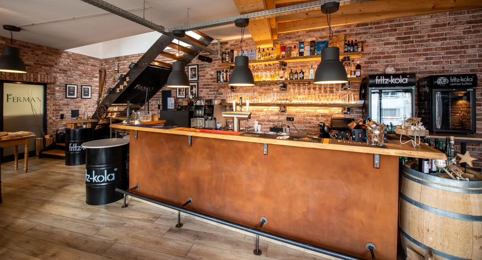 Eine Bar im leichten Industriestil  mit einer roten Klinkerwand. Die Ziegelriemchen passen toll zum Holzboden.