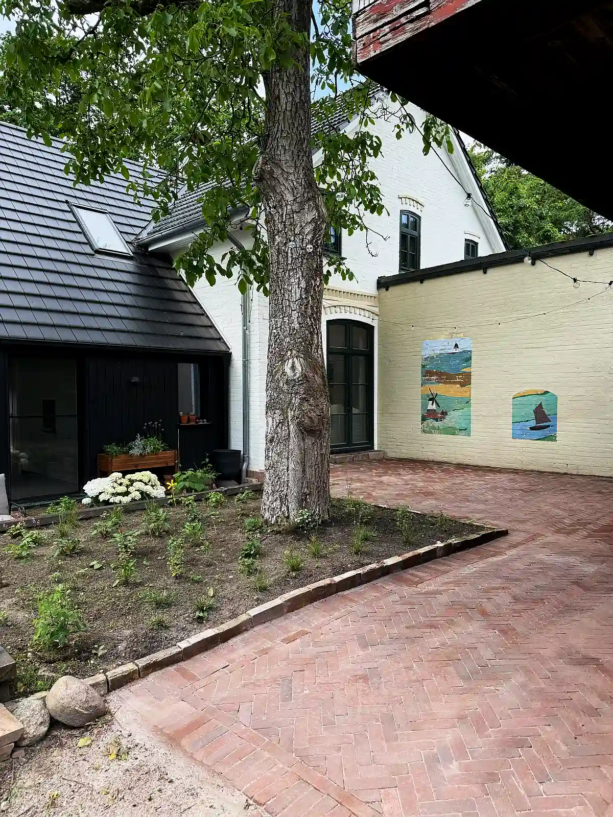 Ein Innenhof mit einem roten Pflasterklinker auf einer Terrasse verlegt. Zentral in der Mitte steht ein Baum.