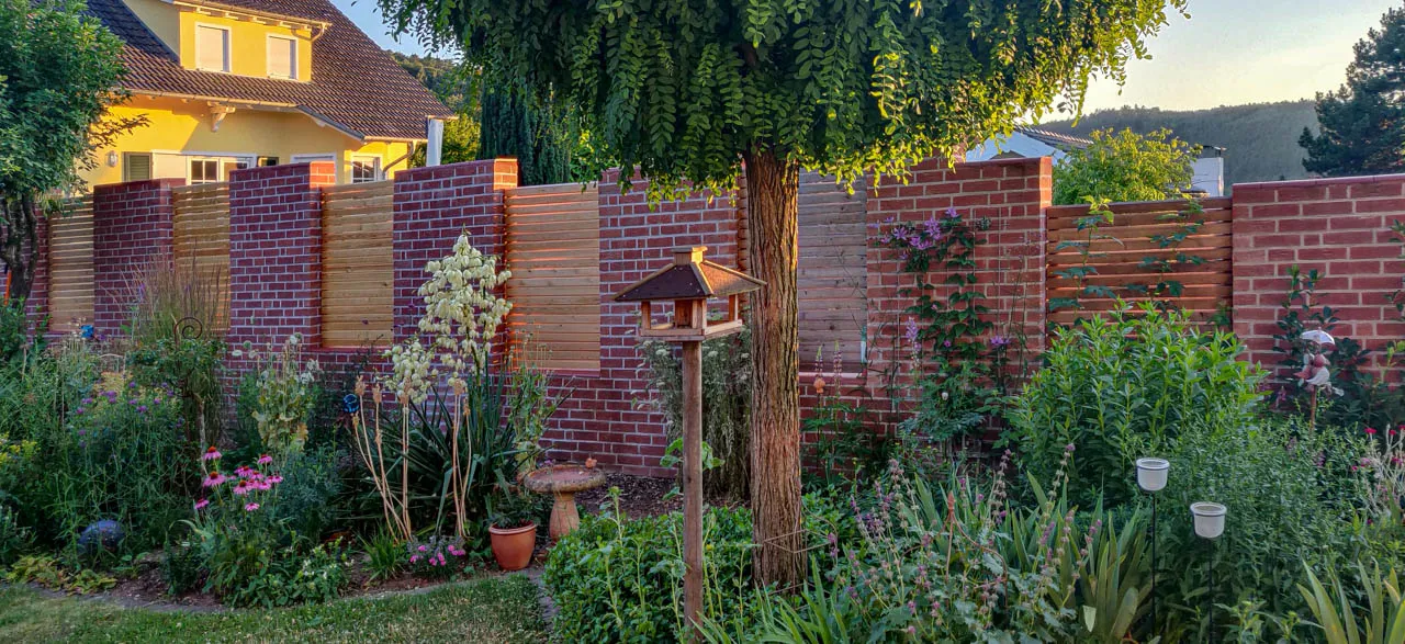 Sichtschutzzaun im Garten aus Kombination mit Holz-Sichtschutz und Klinkermauer im klaren rotton. Mit der grünen Bepflanzung eine schöne klassische dennoch modern wirkende mauer