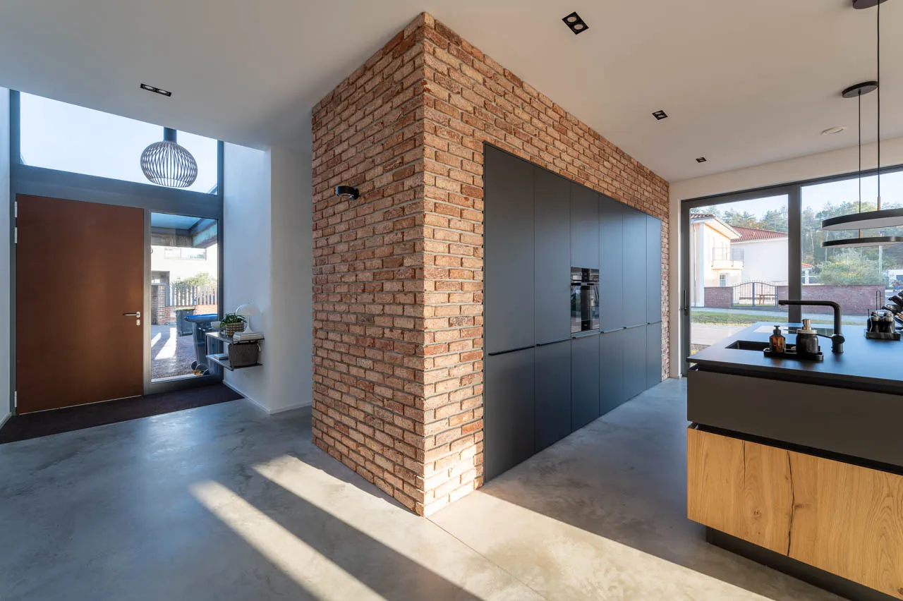 Hochmoderne Küchenwand aus Klinkerriemchen. Die Wand rahmt eine moderne graue Küche ein. Der kontrast zu den edlen roten Riemchen ein echter hingucker