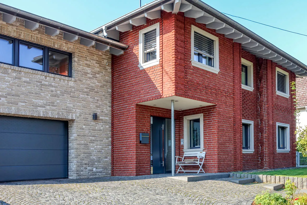 Klassisch rotes Klinkerhaus mit Anbau. Die rotgeflammten Backsteinriemchen kommen mit den weißen Fenstern gut zur Geltung. Der Anbau wurde mit der Sorte Antik vintage verarbeitet, ein grau gehaltenes Riemchen.
