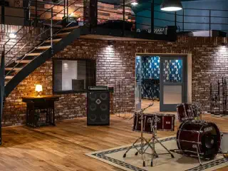 Tonstudio mit Boxen und Schlagzeug im Vordergrund. Die Wände drumherum sind alle verklinkert