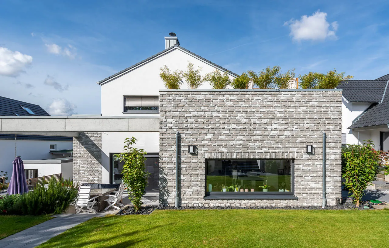 Modernes Haus mit Klinker-Anbau. Die grau, beigen Riemchen mit weißer Schlämme sind hell und modern in hellem Grauton. passen sich gut zur weißen Hausfarbe an und zu dunkel grauen Fenstern